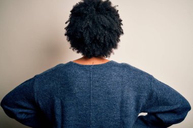 Kıvırcık saçlı, sıradan bir kazak giyen, kolları vücudunda geriye doğru bakan güzel Afro-Amerikan kadın.