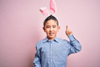 Paskalya tavşanı kulakları takan küçük bir çocuk pembe arka planda başarılı bir fikir işaret ediyor. Heyecanlı ve mutlu. Bir numara..