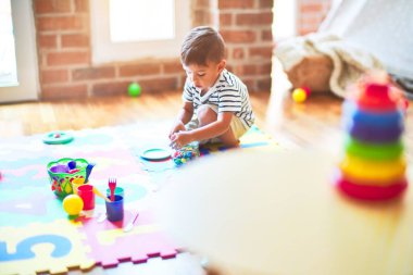 Güzel çocuk bulmacanın üzerinde oturuyor. Anaokulunda plastik tabaklar, meyveler ve sebzelerle oynuyor.