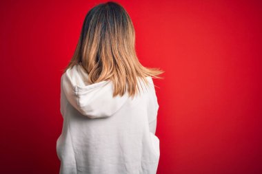 Middle age beautiful sportswoman wearing casual sweatshirt over isolated red background standing backwards looking away with crossed arms
