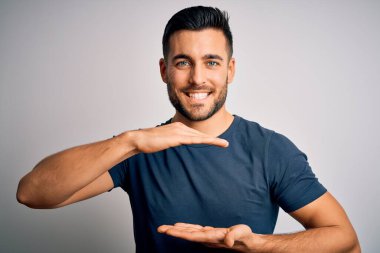 İzole edilmiş beyaz arka plan üzerinde duran, büyük ve büyük beden işareti ve ölçü sembolü gösteren sıradan bir tişört giyen genç yakışıklı bir adam. Kameraya bakıp gülümsüyor. Ölçüm konsepti.