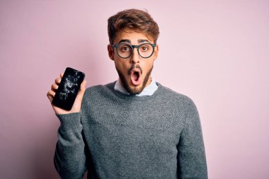 Sakallı, gözlüklü, kırık ve çatırdayan akıllı telefonlu genç adam şaşırmış bir yüzle korkmuş ve korku ifadesinden heyecanlanmış.
