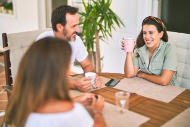 Güzel bir aile terasta oturmuş kahve içiyor, konuşuyor ve gülümsüyor.
