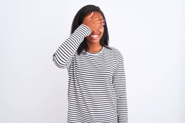 Gülümsüyor ve gözleri için sürpriz kapsayan yüz el ile gülüyor izole arka plan üzerinde kış kazak giyen güzel genç Afro-Amerikan kadın. Kör kavramı.