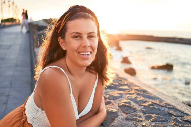 Güzel genç bir kadın kumsalda yürüyor okyanus manzarasının tadını çıkarıyor yaz tatilinde gülümsüyor.