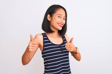 İzole edilmiş beyaz arka planda duran çizgili tişört giyen genç Çinli kadın el hareketini onaylıyor, gülümsüyor ve başarı için mutlu. Kazanan jest.