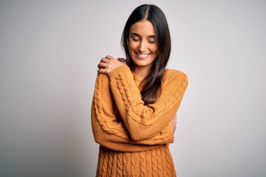Young beautiful brunette woman wearing casual sweater over isolated white background Hugging oneself happy and positive, smiling confident. Self love and self care
