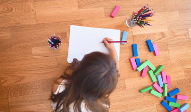 Anaokulunda kağıt ve kalemle yere yatıp resim yapan sevimli çocuk.