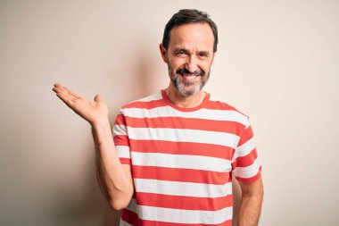 Middle age hoary man wearing casual striped t-shirt standing over isolated white background smiling cheerful presenting and pointing with palm of hand looking at the camera.
