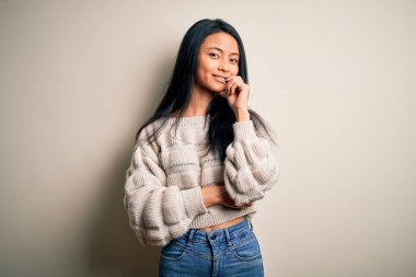 İzole edilmiş beyaz arka plan üzerine günlük süveter giyen genç ve güzel Çinli kadın kameraya kollarını kavuşturup gülümseyerek ve çenesini kaldırarak bakıyor. Olumlu düşünüyorum..