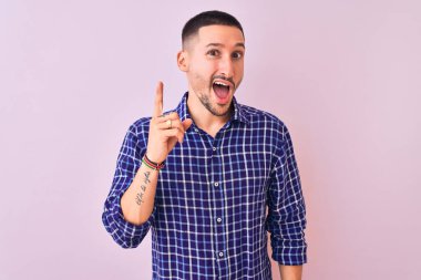 Tecrit edilmiş arka planda duran yakışıklı genç adam başarılı bir fikir işaret ediyor. Heyecanlı ve mutlu. Bir numara..