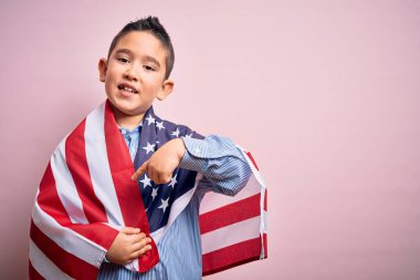Amerika Birleşik Devletleri bayrağına sarılı küçük vatansever çocuk bağımsızlık gününde elini ve parmağını göstererek çok mutlu olur.