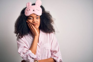 Young african american woman with afro hair wearing sleeping eye mask and pink pajama thinking looking tired and bored with depression problems with crossed arms.