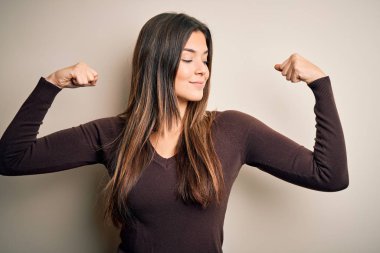 İzole edilmiş beyaz arka plan üzerinde sıradan bir süveter giyen genç ve güzel bir kız gururla gülümseyen kol kaslarını gösteriyor. Fitness konsepti.