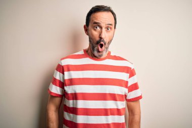 Middle age hoary man wearing casual striped t-shirt standing over isolated white background afraid and shocked with surprise expression, fear and excited face.