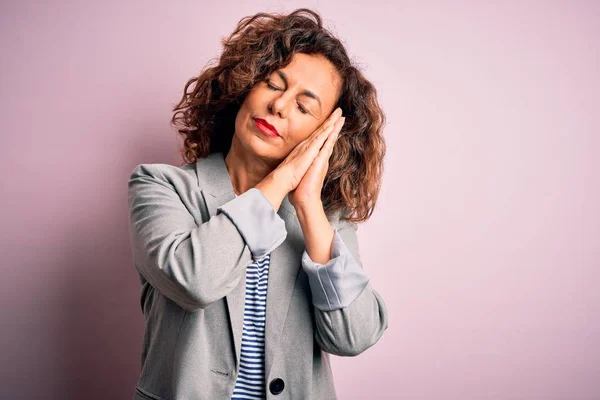 Middle age beautiful businesswoman wearing elegant jacket over isolated pink background sleeping tired dreaming and posing with hands together while smiling with closed eyes.