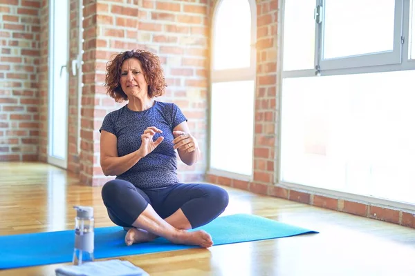 Middle age beautiful sportswoman wearing sportswear sitting on mat practicing yoga at home disgusted expression, displeased and fearful doing disgust face because aversion reaction. With hands raised. Annoying concept.