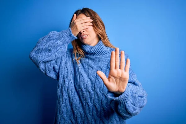 Young beautiful brunette woman wearing casual turtleneck sweater over blue background covering eyes with hands and doing stop gesture with sad and fear expression. Embarrassed and negative concept.