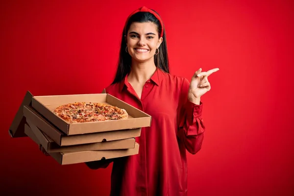 若いです美しいですブルネット女性保持デリバリーボックスとともにイタリアのピザ以上赤背景非常に幸せなポインティングとともに手と指へザ側 — ストック写真