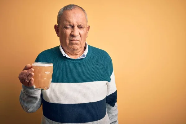 Senior handsome man drinking jar of beer standing over isolated yellow background depressed and worry for distress, crying angry and afraid. Sad expression.