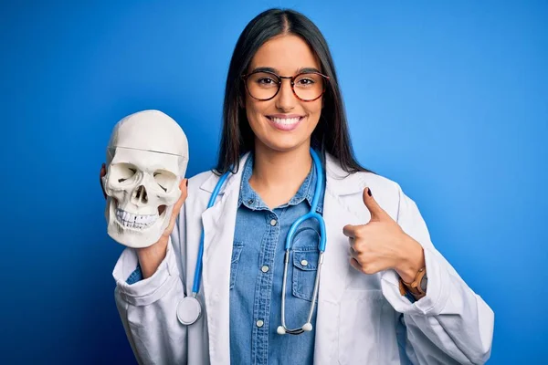 Young Beautiful Brunette Doctor Woman Wearing Coat Holding Human Skull — ストック写真