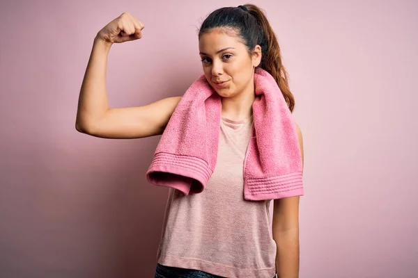 ピンクの背景にスポーツウェアとタオルを身に着けている若い美しいブルネットのスポーツ女性腕の筋肉を示す強い人 自信と力の誇り — ストック写真