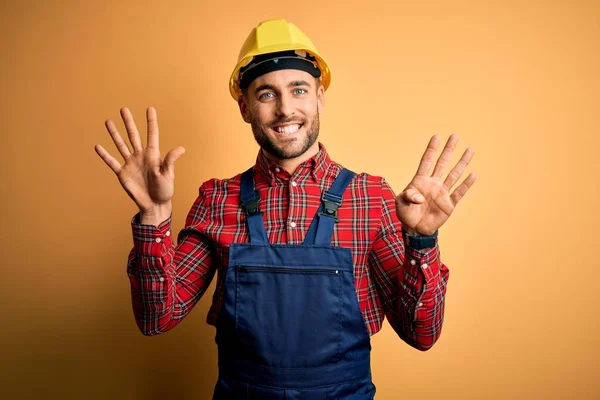 年轻的建筑工人身穿建筑制服 头戴安全帽 头戴黄色的隔离背景 带着九号手指 面带微笑 自信而快乐 — 图库照片