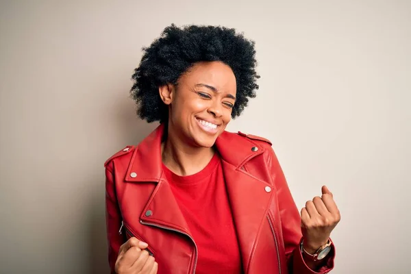 カジュアルな赤いジャケットを着て巻き毛を持つ若い美しいアフリカ系アメリカ人アフロ女性は非常に満足し 腕を上げて勝者のジェスチャーを行う興奮し 笑顔と成功のために叫んでいます お祝いのコンセプト — ストック写真