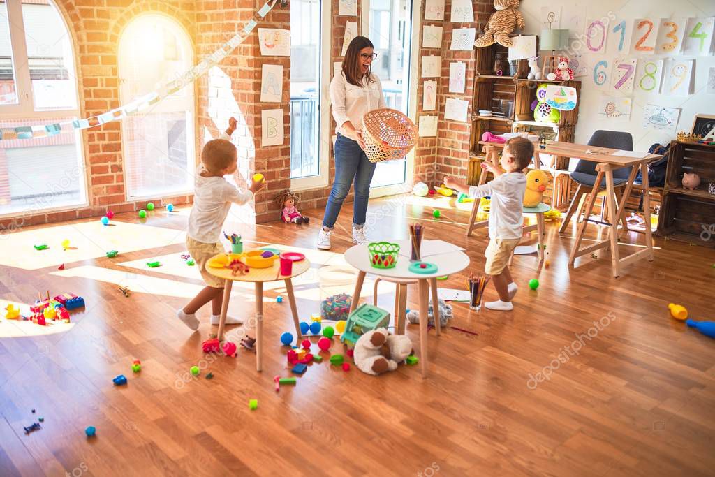 Beautiful teacher and toddlers playing basketball using balls and wicker basket  around lots of toys at kindergarten