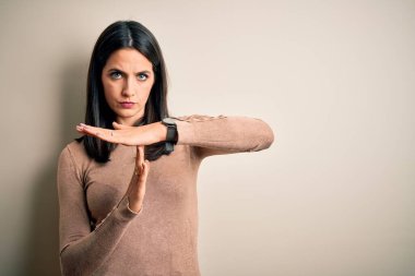 Mavi gözlü genç esmer kadın izole edilmiş beyaz arka plan üzerine günlük süveter giyiyor. Elleriyle jest yapıyor, hayal kırıklığına uğramış ve ciddi bir yüz ifadesi var.