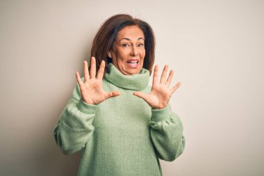 Orta yaşlı, güzel bir kadın izole edilmiş beyaz arka plan üzerine balıkçı yaka kazak giyiyor korku ifadesinden korkuyor ve dehşete düşüyor. El hareketlerini durdur, şok içinde bağır. Panik konsepti.