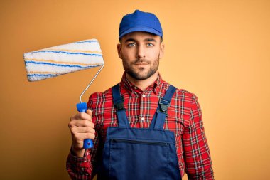 Genç yakışıklı ressam duvarları boyuyor. İzole edilmiş sarı arka plan üzerinde yuvarlak bir araç kullanıyor. Akıllı bir yüz ifadesiyle ciddi ciddi düşünüyor.