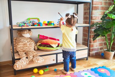 Güzel çocuk anaokulunda oyuncaklarını rafa kaldırıyor.