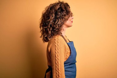 Orta yaşlı, güzel fırıncı kadın, önlük takıyor, izole edilmiş sarı arka planda duruyor, yan yana bakıyor, rahat poz veriyor, kendine güvenen bir gülümsemeyle doğal bir yüz ifadesi var..