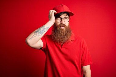 Gözlüklü ve kırmızı şapkalı genç teslimatçı. Alnındaki sorun yüzünden endişeli ve stresli. Kriz için endişeli.