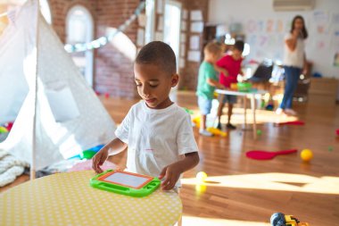 Anaokulunda bir sürü oyuncakla oynayan genç ve güzel öğretmen ve çocuklar.