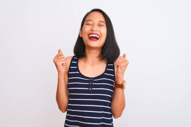 İzole edilmiş beyaz arka planda duran çizgili tişört giyen genç Çinli kadın. Kolları havada ve gözleri kapalı zaferi kutlarken gülümsüyor. Kazanan konsept.