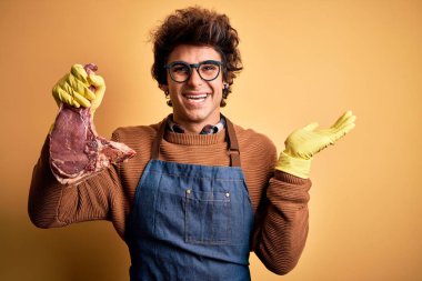 Genç yakışıklı kasap biftekle karşılaşıyor. Sarı arka planda duruyor. Gülümsüyor, avucunun içi gibi kameraya bakıyor..