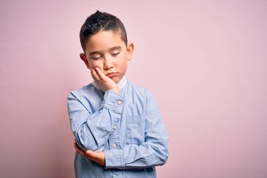 Pembe izole edilmiş arka planda duran zarif tişörtlü genç çocuk kollarını kavuşturarak depresyondan sıkılmış ve yorgun görünüyor..
