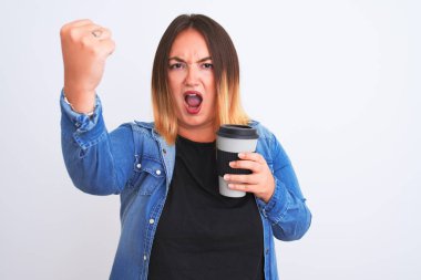 Genç, güzel bir kadın izole edilmiş beyaz arka planda bir bardak kahve içerken sinirlenmiş ve sinirlenmiş bir şekilde bağırıyor, çıldırmış ve el kaldırarak bağırıyor.