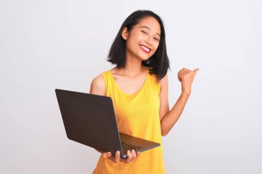 Genç, güzel Çinli bir kadın dizüstü bilgisayar kullanıyor. İzole edilmiş beyaz arka plan üzerinde duruyor. Kocaman gülümsüyor.