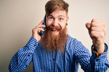 Kızıl saçlı, sakallı İrlandalı bir adam akıllı telefondan konuşuyor izole bir arka planda gururla bağırıyor ve zaferi ve başarıyı kutluyor çok heyecanlı, coşkulu bir duygu.