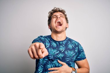 Tatilde, kıvırcık saçlı, yaz tişörtü giyen, sana gülen, eli vücudunun üzerinde kamerayı işaret eden, utangaç yüzlü genç sarışın adam.