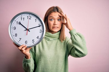 İzole edilmiş pembe arka planda nöbet tutan genç ve güzel bir kadın. Elleri başının üstünde, utanç ve şaşkınlık dolu, sinirli ve hayal kırıklığına uğramış bir halde. Hata için korku ve üzüntü.