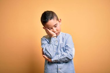 Young little boy kid wearing elegant shirt standing over yellow isolated background thinking looking tired and bored with depression problems with crossed arms.