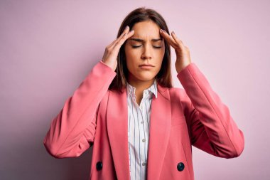 Young beautiful brunette woman wearing jacket standing over isolated pink background with hand on head for pain in head because stress. Suffering migraine.