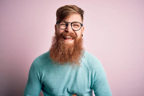 英俊潇洒的爱尔兰红头发男人 留着胡子 戴着眼镜 戴着粉色的隔离背景 笑得很开心 笑得很大声 因为一个滑稽的疯狂笑话 双手放在身上 — 图库照片