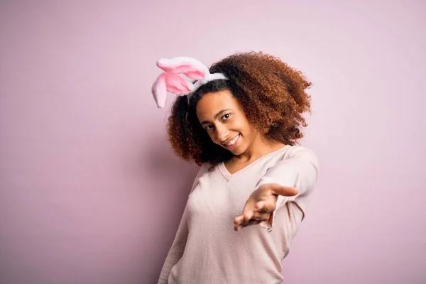 年轻的非洲裔美国女人 一头黑发 长着小兔子耳朵 背景粉红 笑容可亲 手牵手给予帮助和接纳 — 图库照片