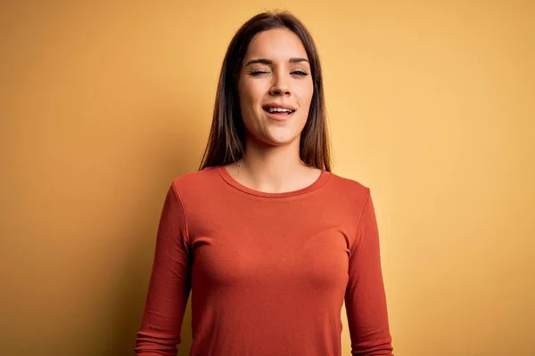 Young beautiful brunette woman wearing casual t-shirt standing over yellow background winking looking at the camera with sexy expression, cheerful and happy face.