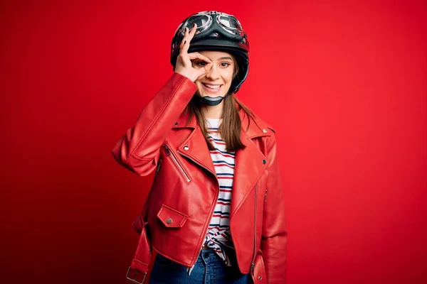若いです美しいですブルネットMotocylistist女性身に着けていますオートバイヘルメットと赤いジャケット行いますOkジェスチャーとともに手笑顔 目を通して見る指で幸せな顔 — ストック写真
